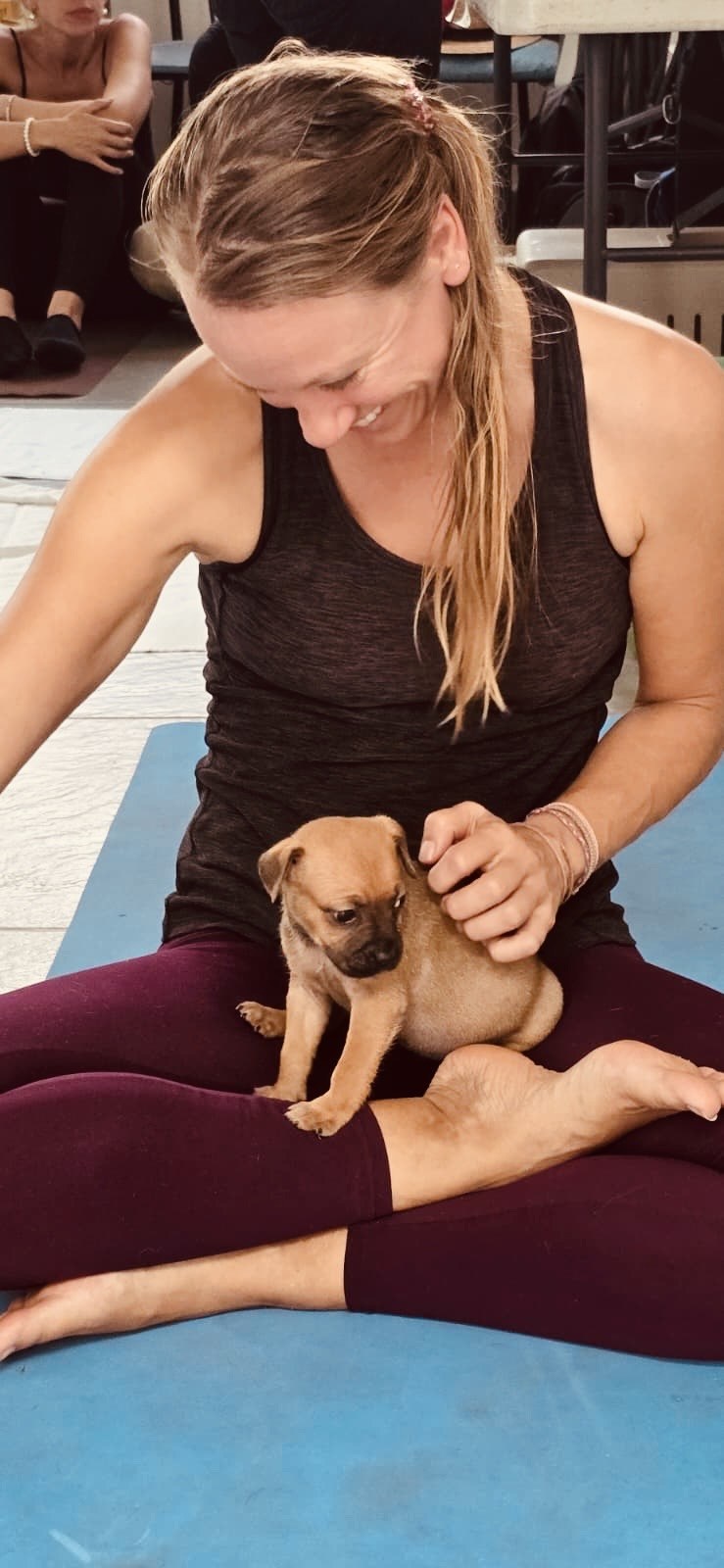 A smiling participant sitting on a yoga mat with a puppy on her lap